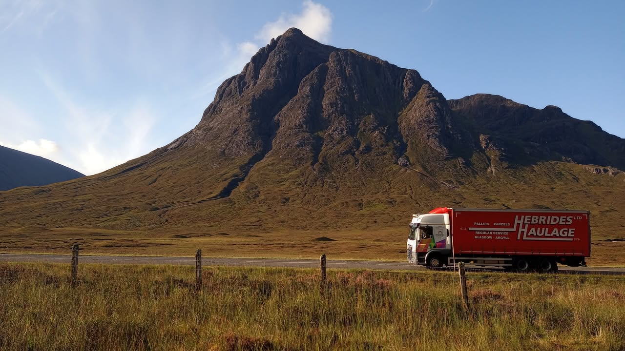 Hebrides Haulage red curtain-sider truck on the road beneath Buachaille Etive Mor in the Scottish Highlands